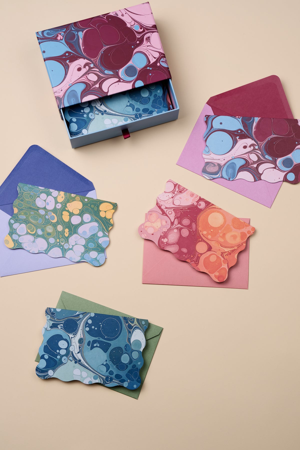 A partially open Boxed Marble Notecard Set - 16 Cards displayed alongside four die-cut cards and their matching colored envelopes.