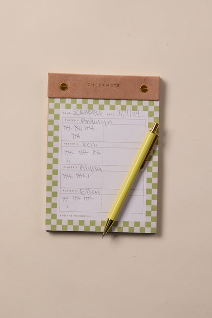 The Check Mate - Game Score Post-Bound Pad features a brown header and handwritten Scrabble scores for four players, with a yellow pen on top. This 4-player score pad rests on a beige surface, ideal for organized scorekeeping.