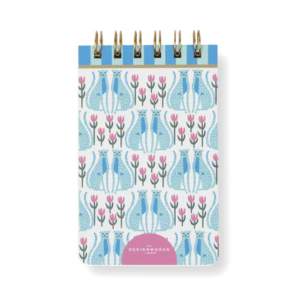 The A Dopo Blue Cheetah Twin Wire Notepad is a small, compact notepad featuring a stylish blue cheetah pattern on the cover, accented with pink details and leaves. A pink semicircle at the bottom displays white “DesignWorks Ink” text, making it an ideal choice for anyone seeking chic and eco-friendly stationery.