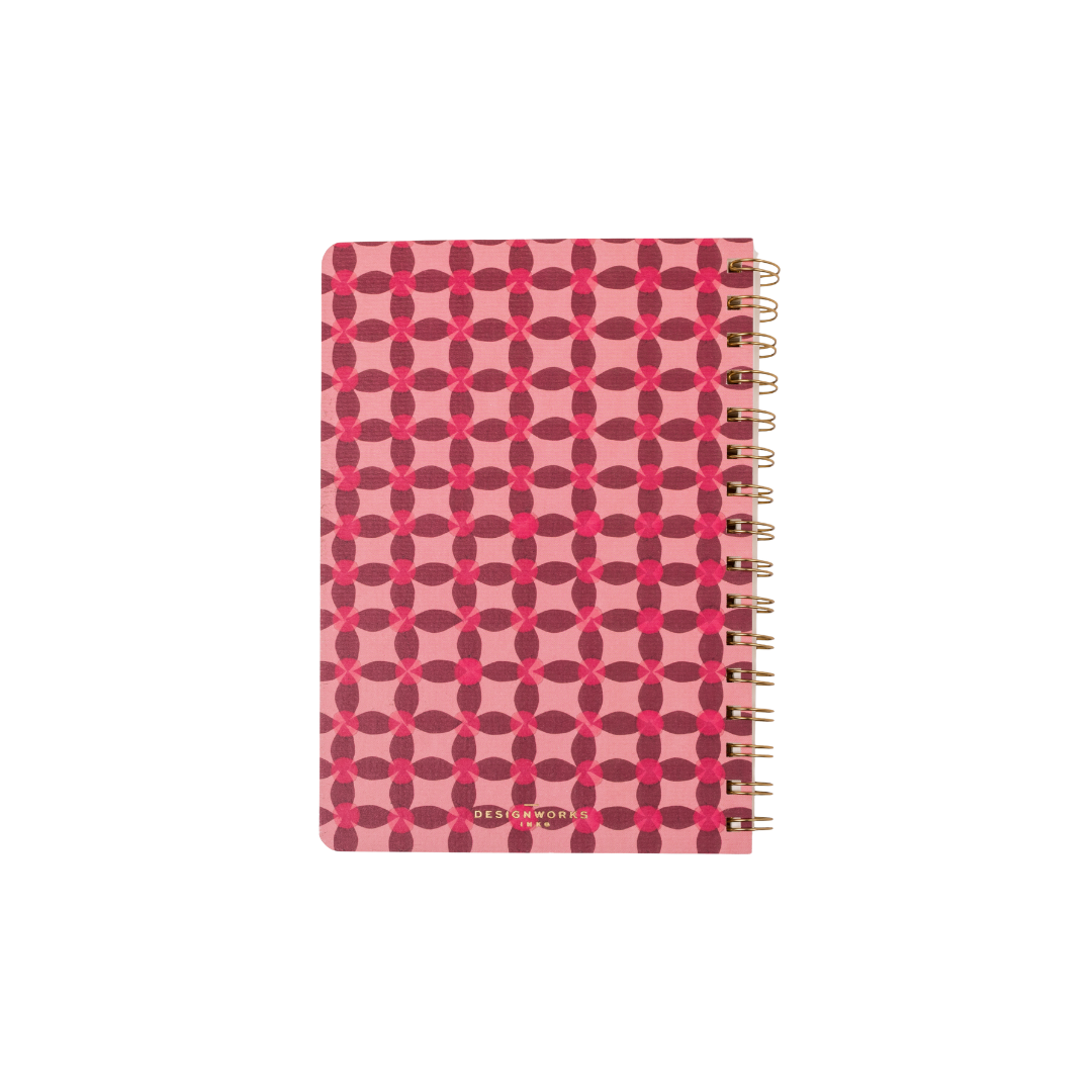 The Tulip Twin Wire Notebook - Small Pinwheel Pink is spiral-bound with a pink cover decorated with red circles and intersecting lines, gold binding on the right side, and perforated pages for easy removal.