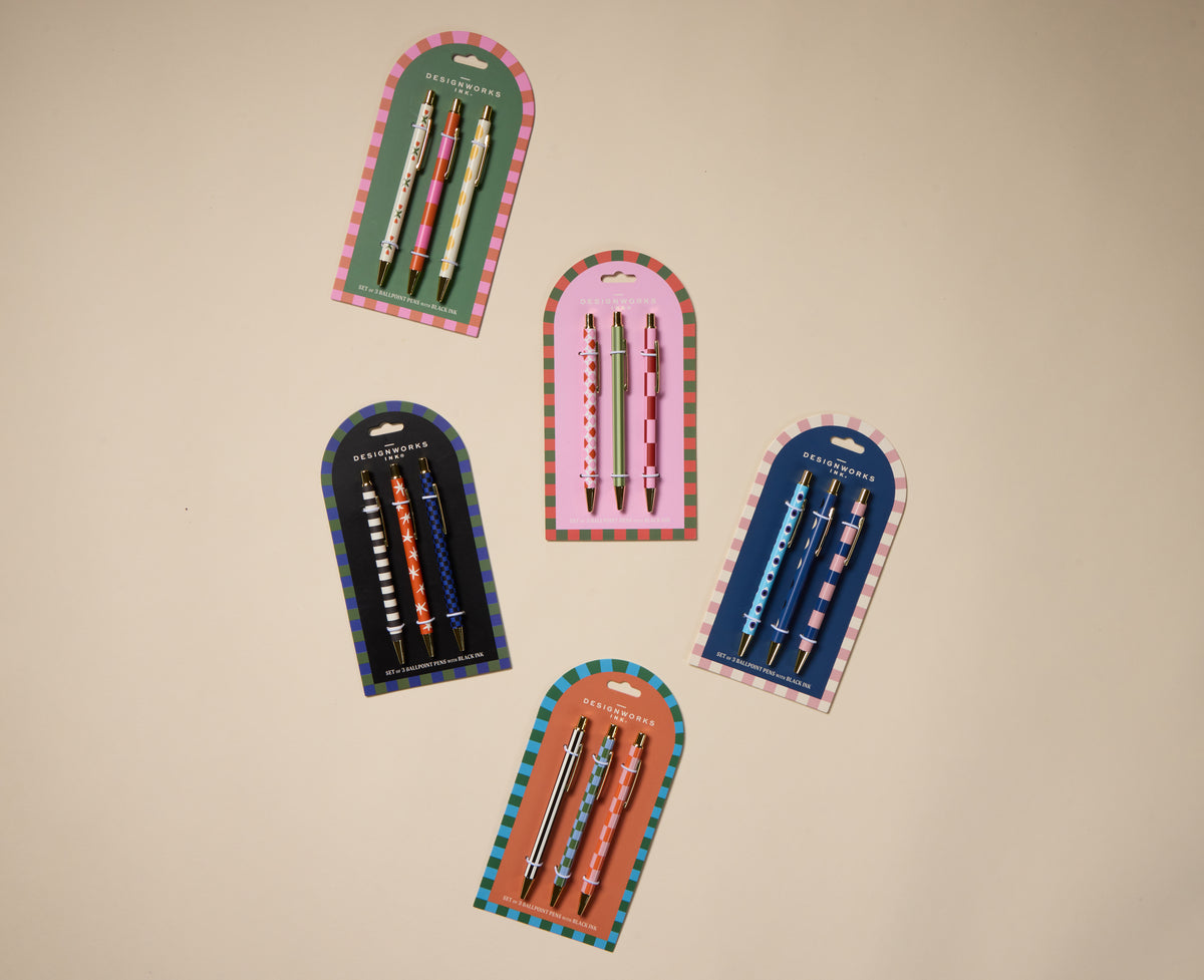Three packs of A Dopo pens—Stripe, Star, and Check—are arranged in a loose circle on a beige background. Each pack contains 3 ballpoint pens with unique designs and vibrant colors.