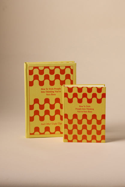 Two yellow How To Trick People Journals with red wavy cover patterns stand upright against a plain beige background.