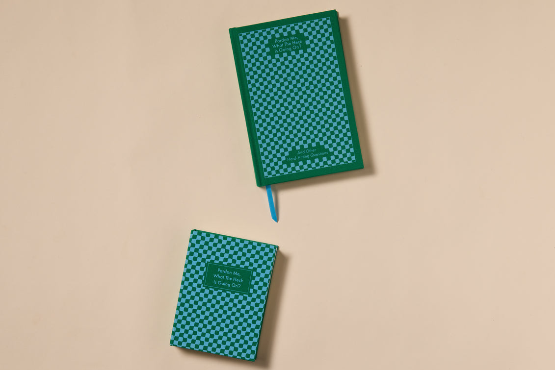 Two green and blue checkered Pardon Me Journals with dark green borders feature bookcloth covers, lay-flat binding, and a blue ribbon bookmark. Both display text in a small green rectangle on the cover, shown on a beige surface.