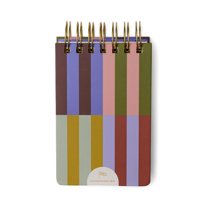 The Chunky Small Twin Wire Notepad - Bold Stripes features a sturdy hard cover decorated with bold vertical and horizontal stripes in green, purple, red, pink, brown, and yellow. Gold twin wire binding secures the top of the 192-sheet pocket notepad, which also displays a small logo at the bottom.
