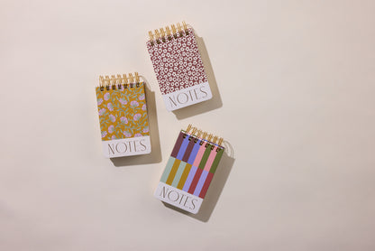 Three Chunky Small Twin Wire Notepads - Bold Stripes are displayed on a light surface. Each small hardcover pocket notebook has 192 sheets and features a distinct design: floral, circular pattern, or colorful vertical stripes.