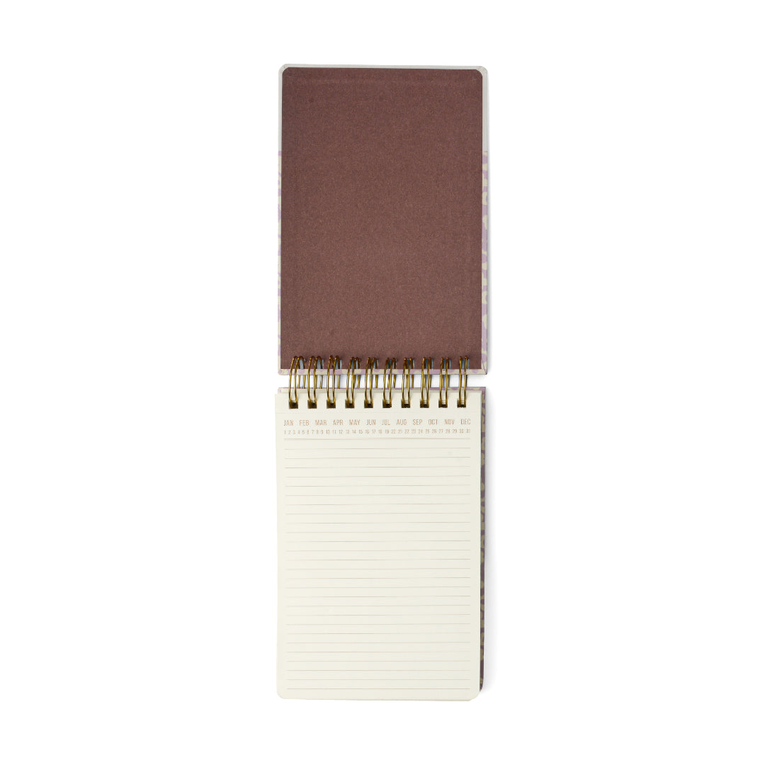 The Chunky Large Notepad - Lilac Groovy Floral features an open spiral-bound design with a sturdy hard cover flipped back, revealing 192 lined cream pages each topped with month abbreviations. Gold wire binding at the center adds both style and practicality to this pocket-friendly notepad.