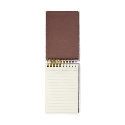 The Chunky Large Notepad - Lilac Groovy Floral features an open spiral-bound design with a sturdy hard cover flipped back, revealing 192 lined cream pages each topped with month abbreviations. Gold wire binding at the center adds both style and practicality to this pocket-friendly notepad.