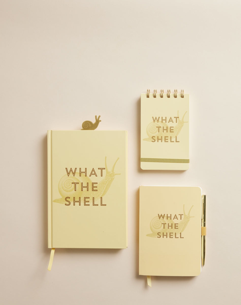 Three Vintage Sass Notepads - What The Shell, each yellow with gold foil accents, a snail illustration, and the phrase WHAT THE SHELL on the cover, are arranged on a beige surface.