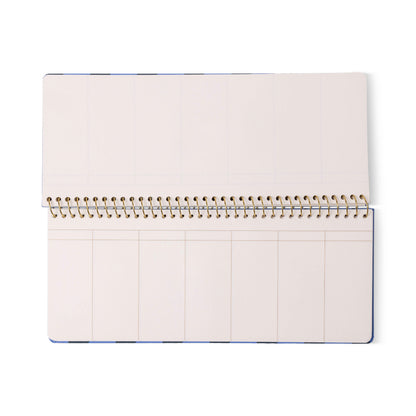 The Color Block Weekly Planner Pad - Blue + Navy features an open, spiral-bound design with undated, blank pages divided into multiple columns and accented with understated gold foil details, lying flat on a white background.