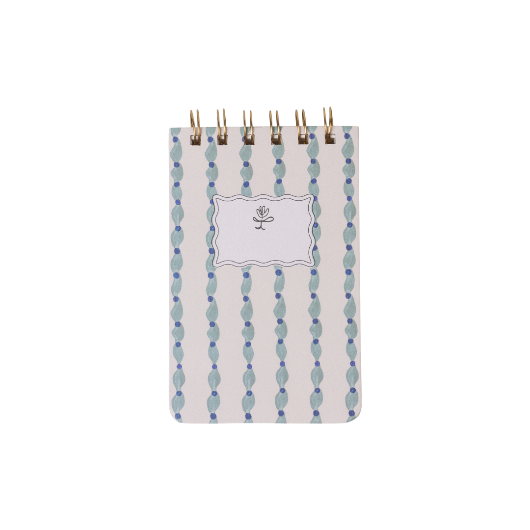 The Tulip Twin Wire Notepad - Wavy Blue is a compact notepad with lined pages, a blue and white wavy pattern cover, and a blank label featuring a simple flower illustration.