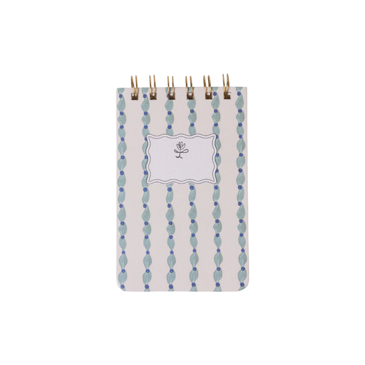 The Tulip Twin Wire Notepad - Wavy Blue is a compact notepad with lined pages, a blue and white wavy pattern cover, and a blank label featuring a simple flower illustration.