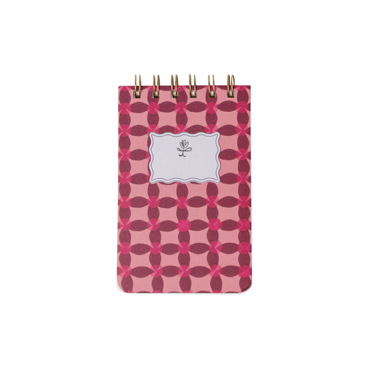 The Tulip Twin Wire Notepad - Pinwheel Pink is a small, spiral-bound notepad with a pink and red geometric cover and a white label with a simple flower drawing.