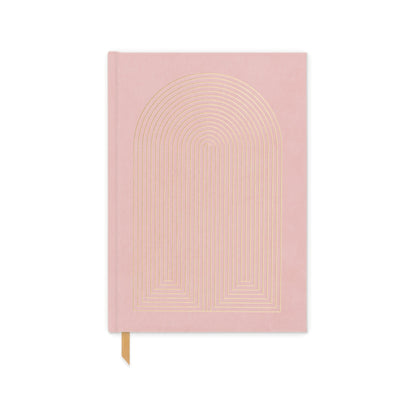 A Hard Cover Suede Cloth Journal With Pocket - Radiant Rainbow, featuring a pink suede cover with a gold geometric arch design and gold ribbon bookmark, is shown against a white background.