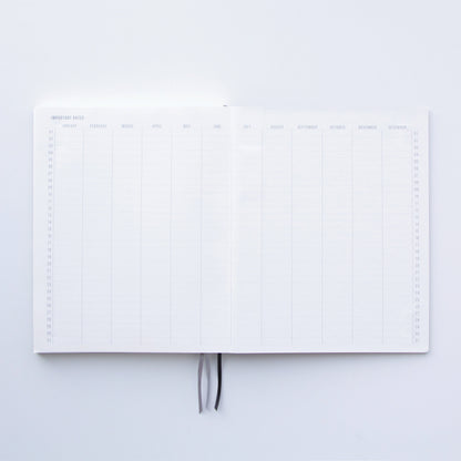 The Standard Issue Notebook No.3 - Green is open to a two-page yearly overview with monthly columns and rows for days 1–31. Two ribbon bookmarks at the center highlight its quality construction and premium writing experience.