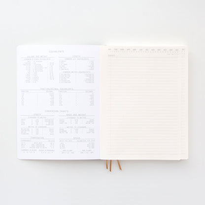 The Standard Issue Project Notebook No.4 - Black features acid-free paper with conversion charts on the left page and a blank lined page on the right, both displayed on a white surface.