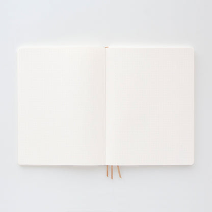 The Standard Issue Project Notebook No.4 - Black, with a flexible cover and light dotted, acid-free pages, lies flat on a white surface, showing two beige ribbon bookmarks.