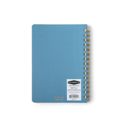 A Medium Blue Textured Paper Twin Wire Notebook with a white label on the back cover displaying product information, photographed on a white background.